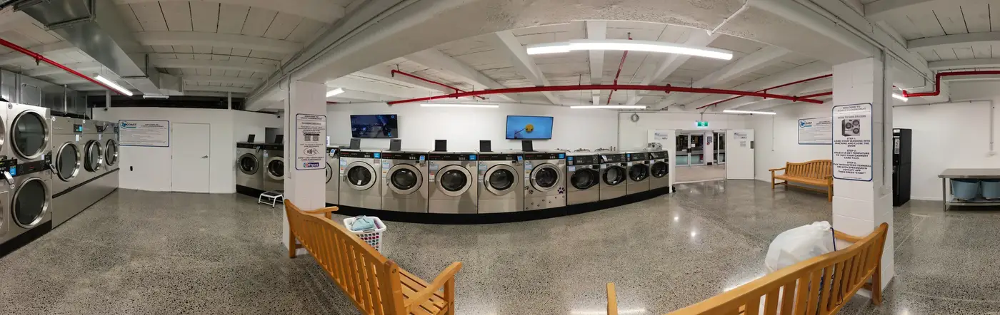 Panorama of the bright, modern interior of Coast Laundromat Whangaparaoa with washers and dryers