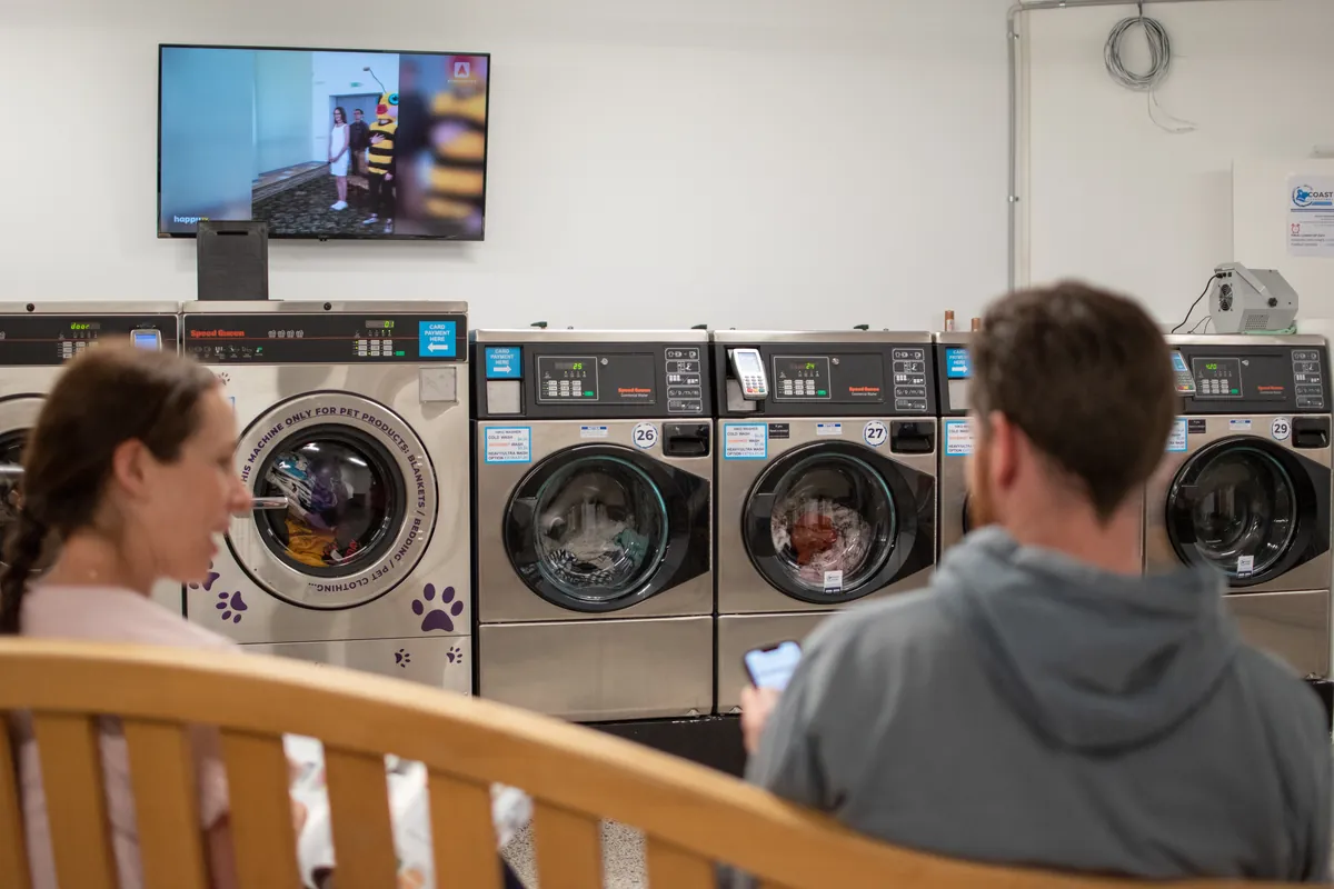 Customers relaxing on the bench while their washing runs at Coast Laundromat Whangaparaoa